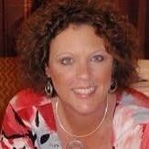 Woman with curly brown hair wearing a floral top and a necklace, smiling.
