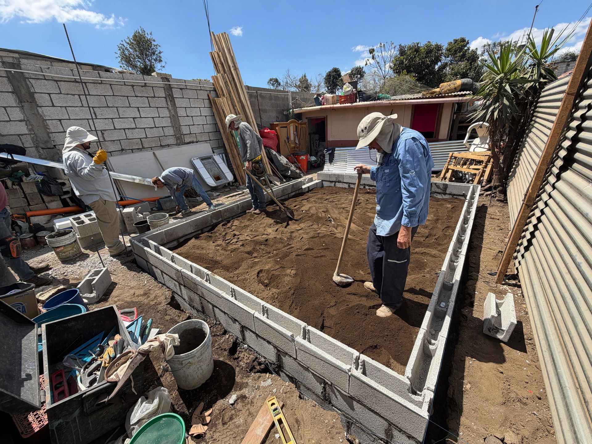 Workers prepare a rectangular concrete foundation filled with soil for a construction project in an outdoor area.