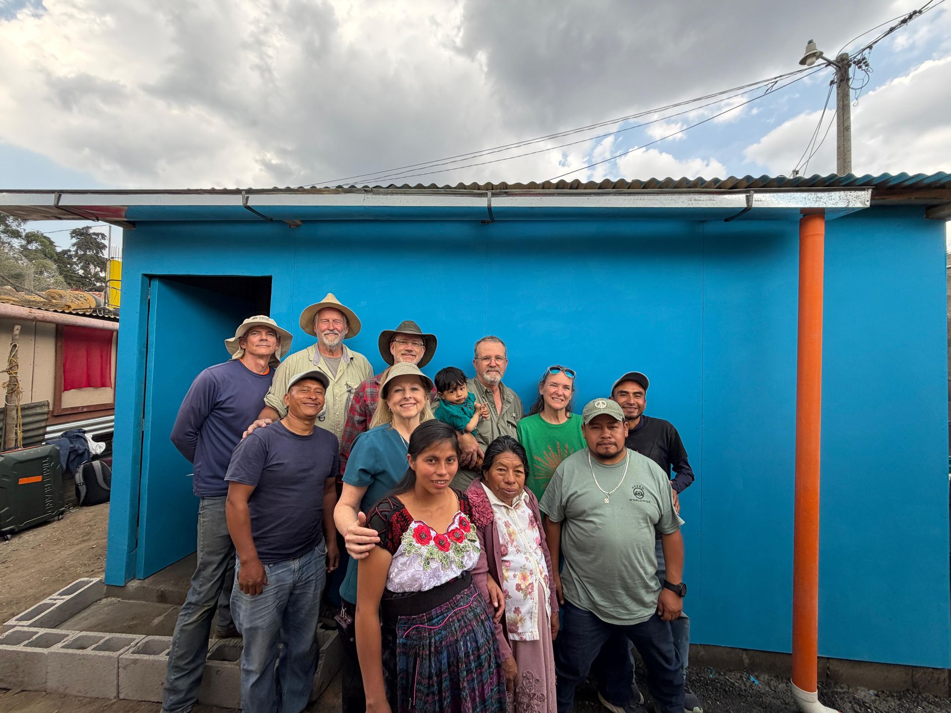 A group stands in front of a bright blue building under a cloudy sky after completing a construction project.