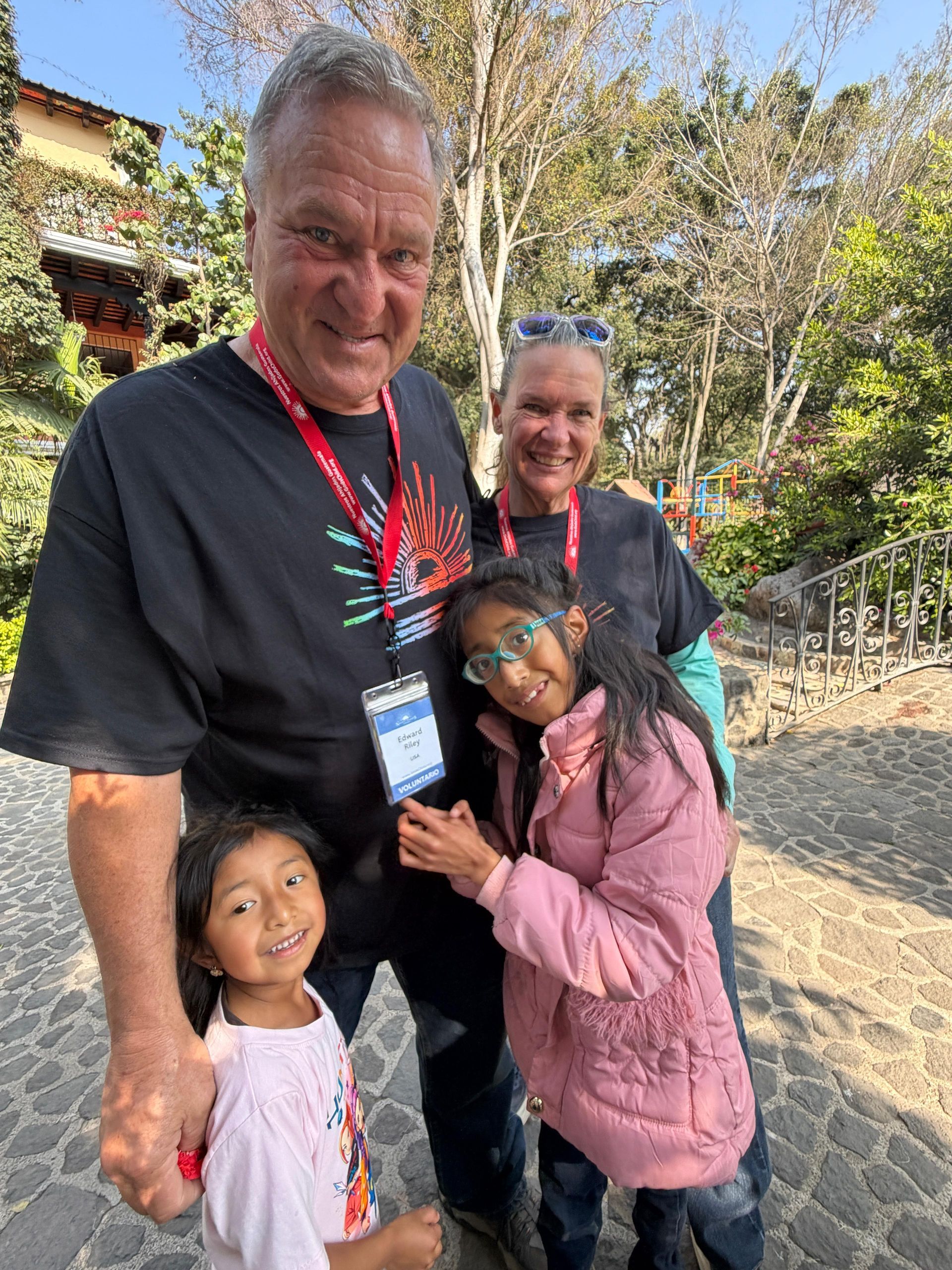 Two adults and two children stand together outdoors on a cobblestone path, smiling toward the camera.