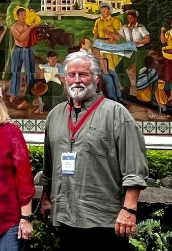 A man with a beard and a name tag on his neck stands in front of a painting