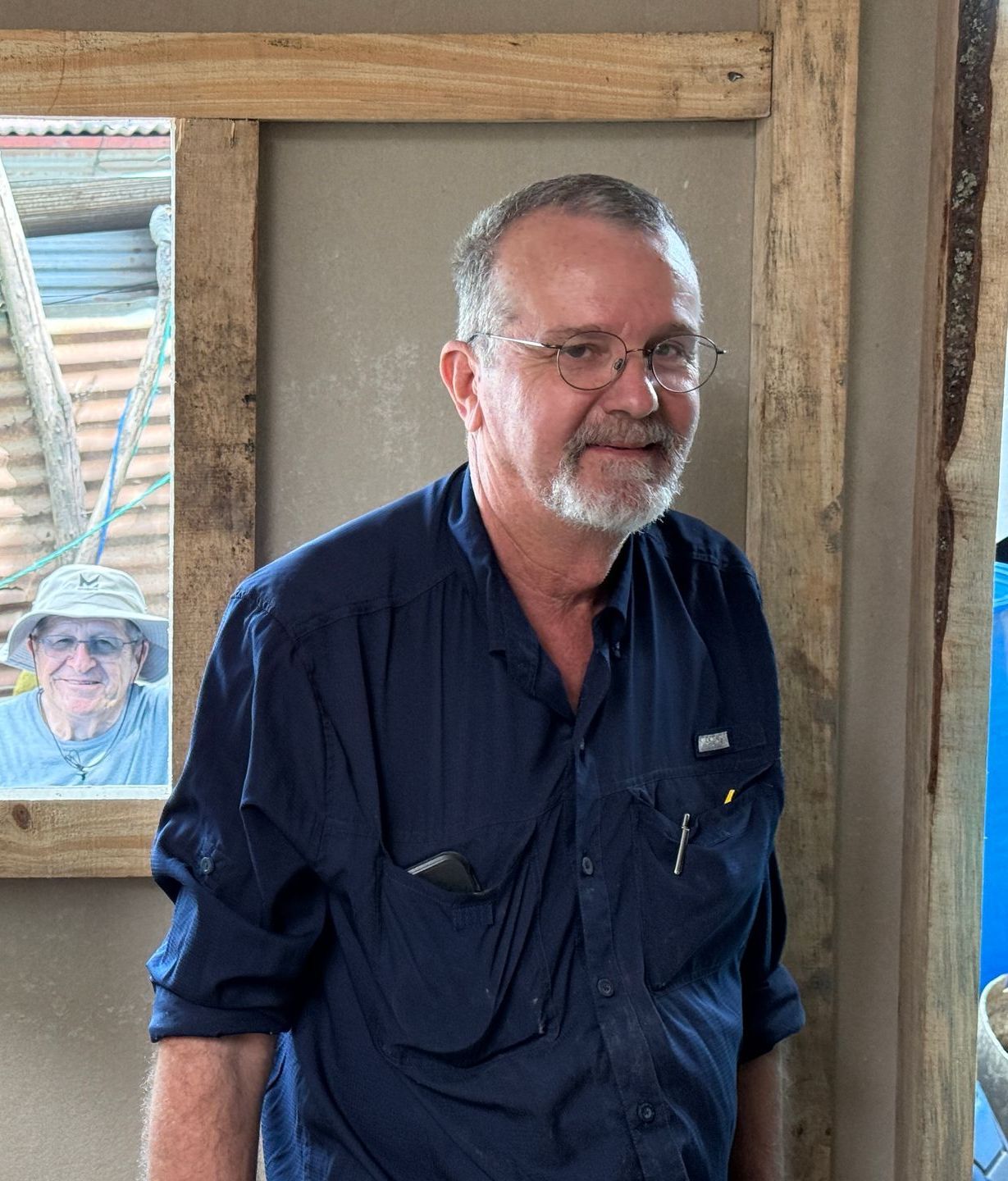 A man in a blue shirt is standing in front of a window.