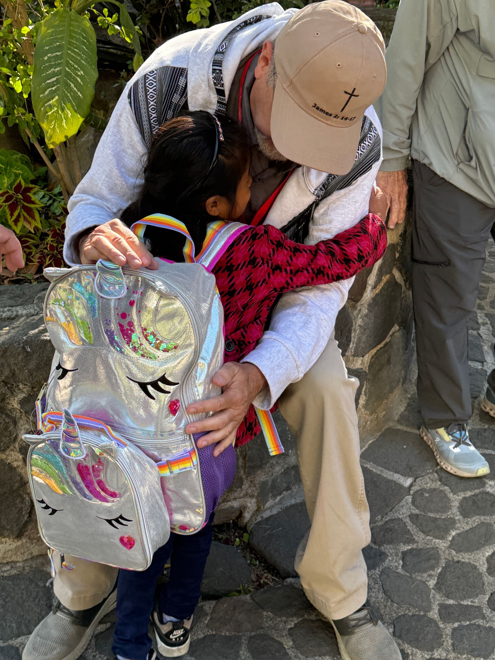 A man is hugging a little girl who is wearing a unicorn backpack.