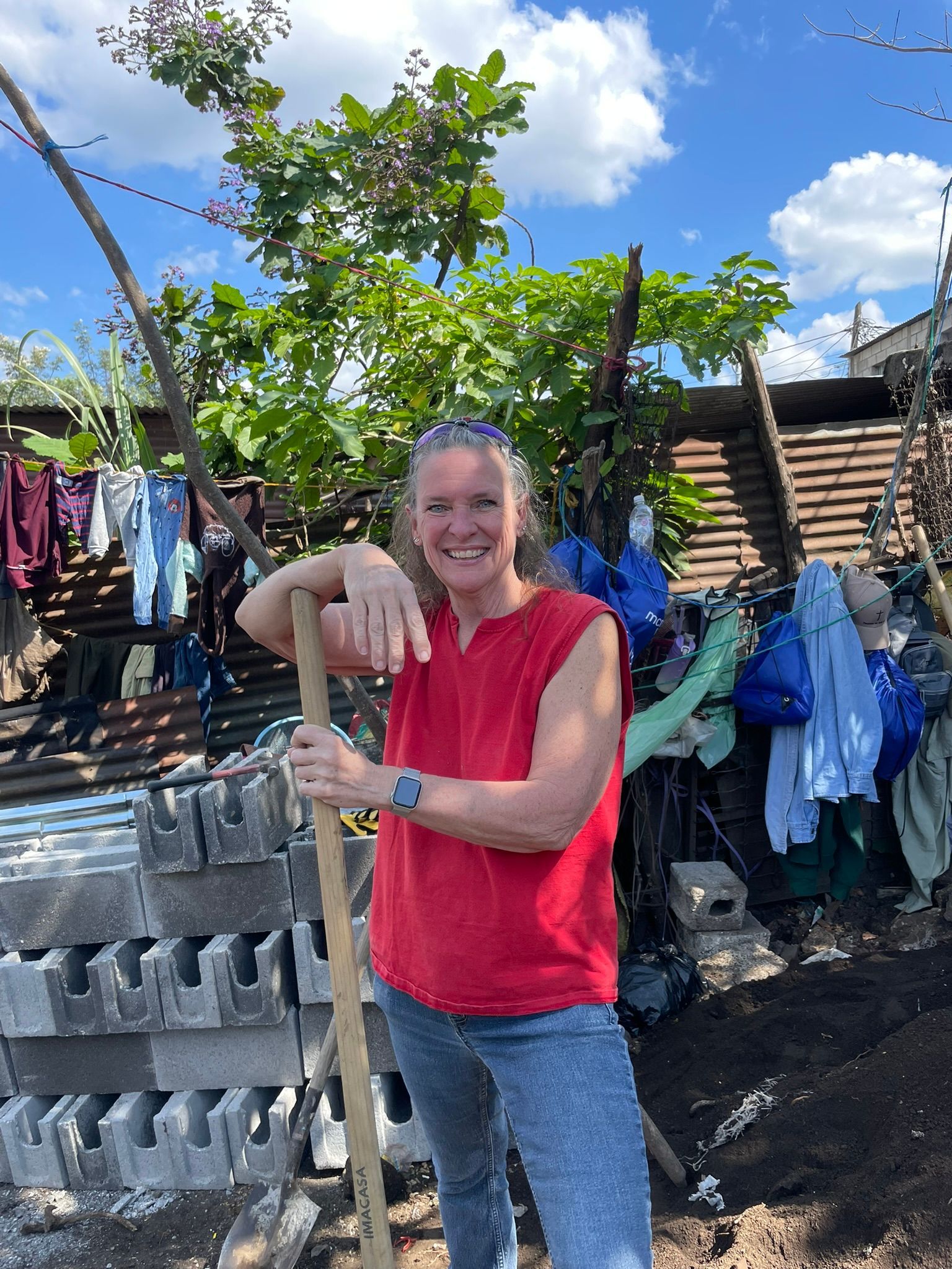 A woman in a red shirt is holding a shovel and smiling.