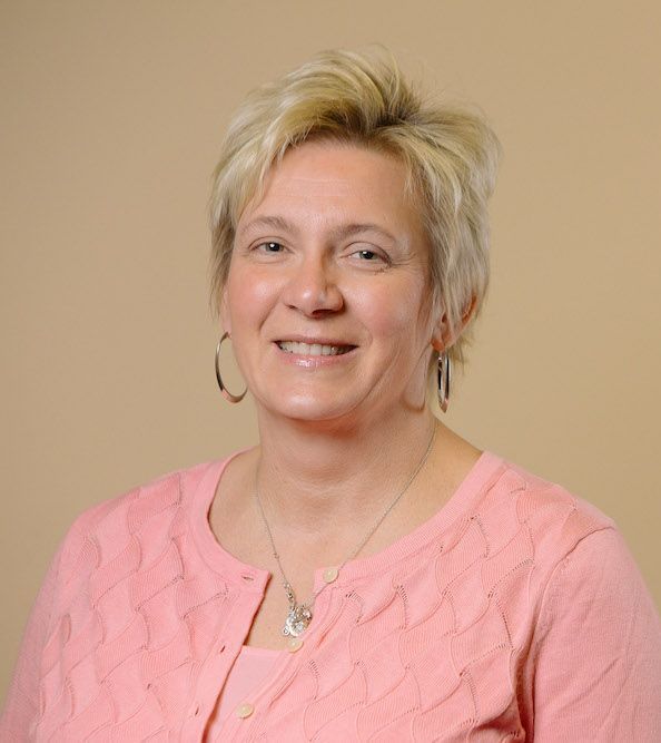 A woman wearing a pink sweater and earrings is smiling for the camera.