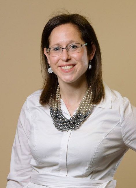 A woman wearing glasses and a pearl necklace is smiling for the camera.