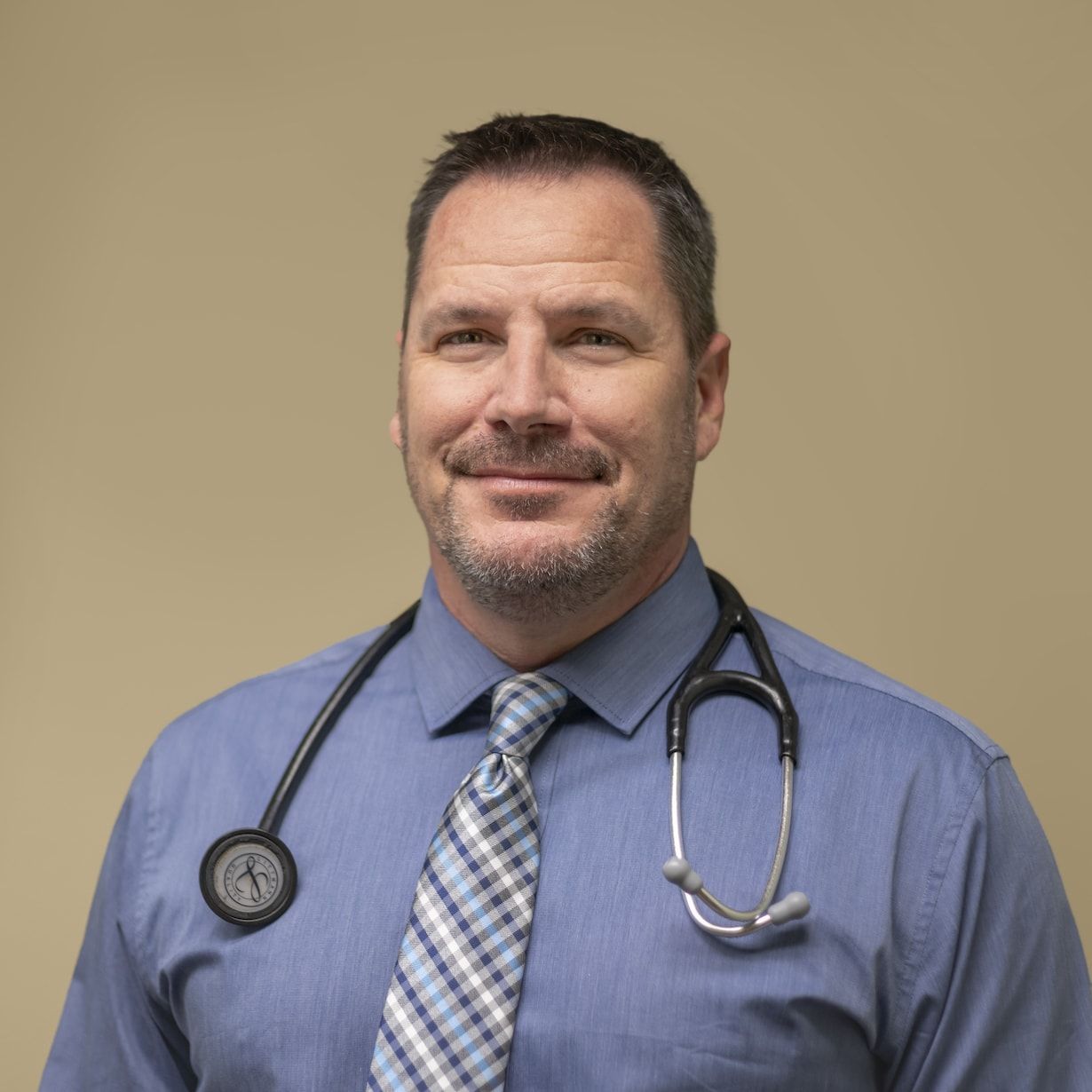 A man wearing a blue shirt and tie with a stethoscope around his neck.