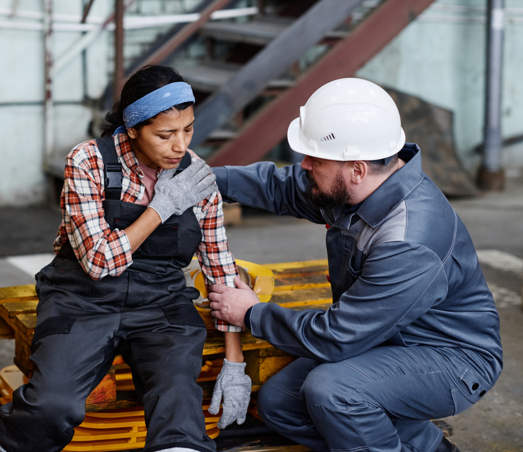 A man in a hard hat is kneeling down next to a woman in overalls.