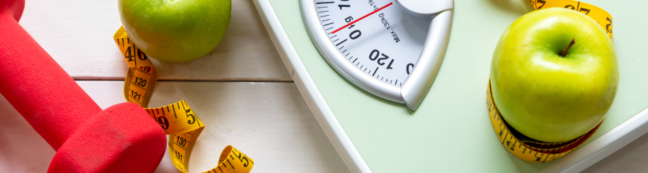 A scale , apples , a measuring tape and a dumbbell are on a table.
