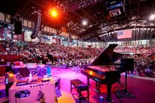 A grand piano is sitting on a stage in front of a crowd at a concert.
