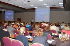 A large group of people are sitting in a conference room watching a presentation.