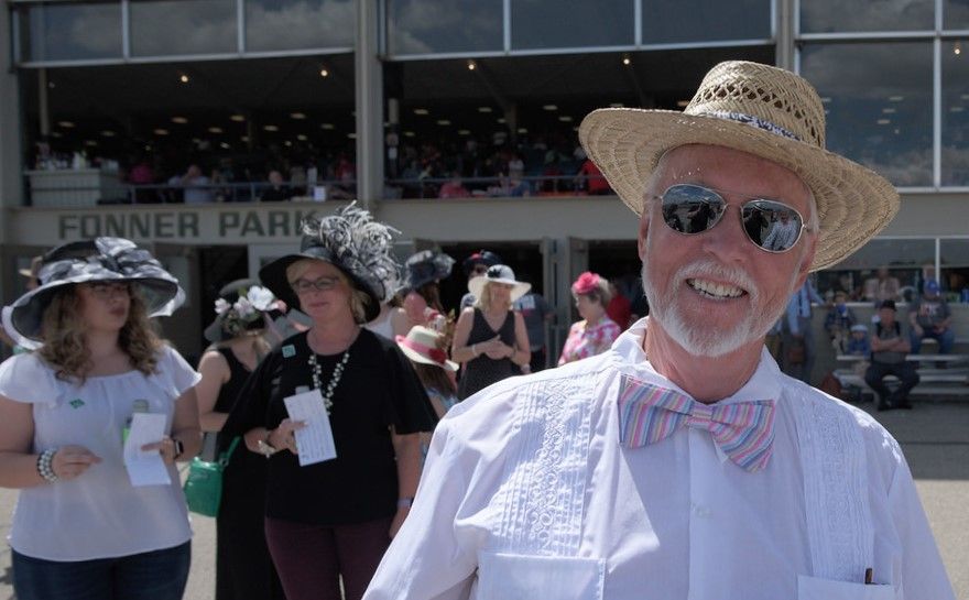 A man wearing a straw hat and bow tie is standing in front of fonner park