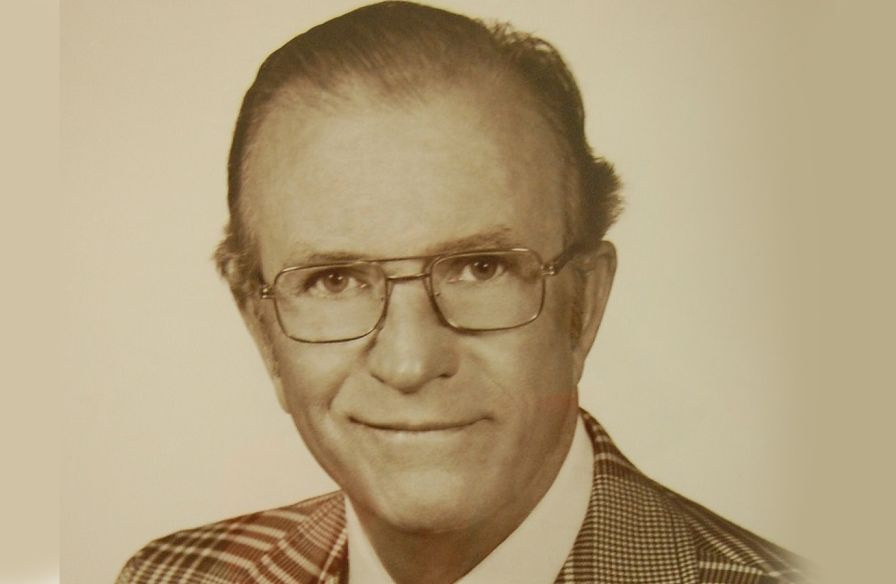 A man wearing glasses and a suit is smiling in a black and white photo.