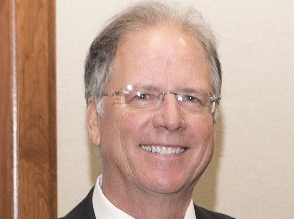 A man wearing glasses and a suit is smiling for the camera.