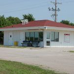 A small white building with a red roof and a bench in front of it.