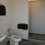 A bathroom with a toilet , sink and paper towel dispenser.