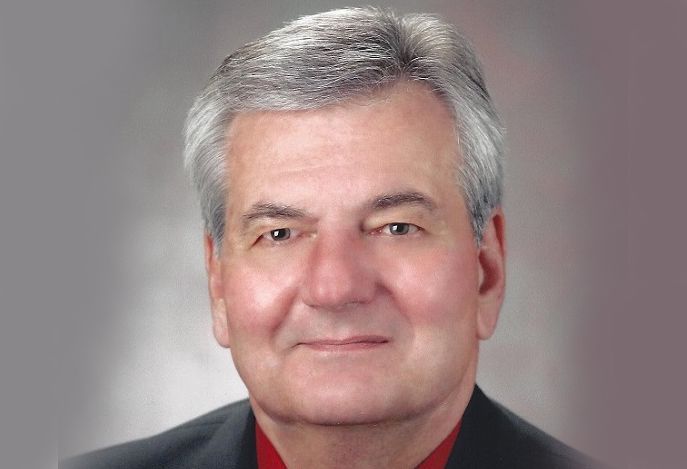 A man in a suit and red shirt is smiling for the camera.