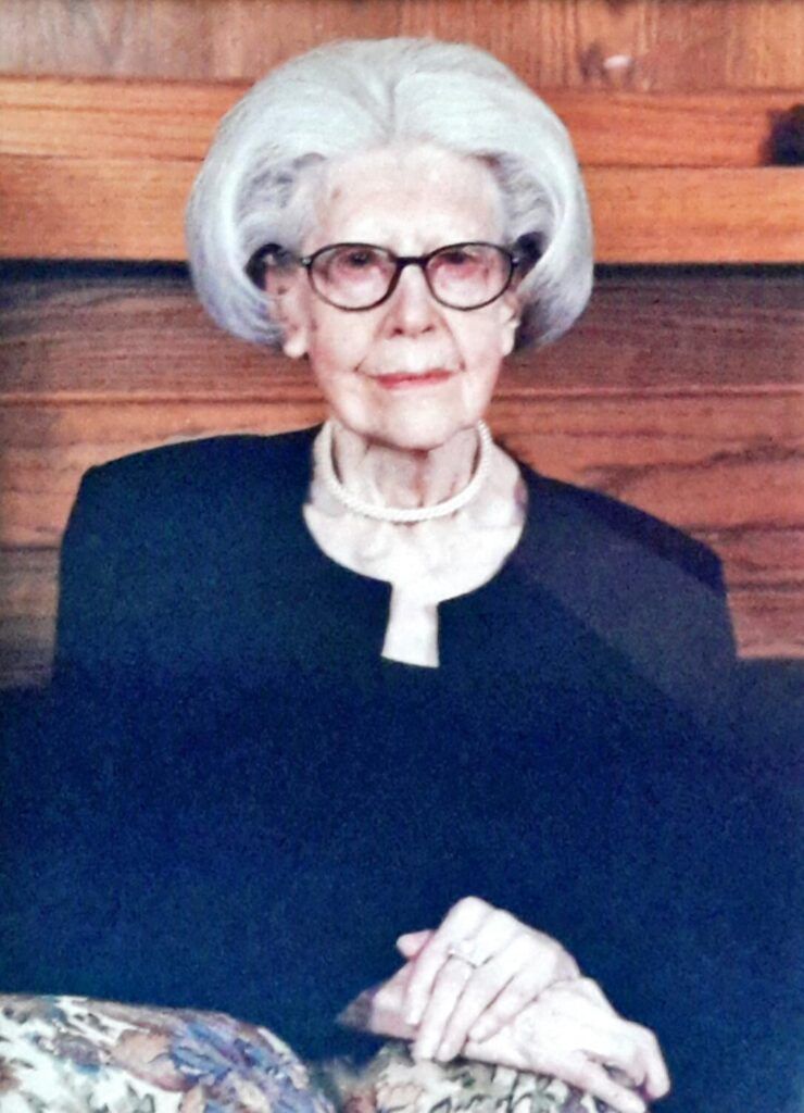An elderly woman wearing glasses is sitting on a couch