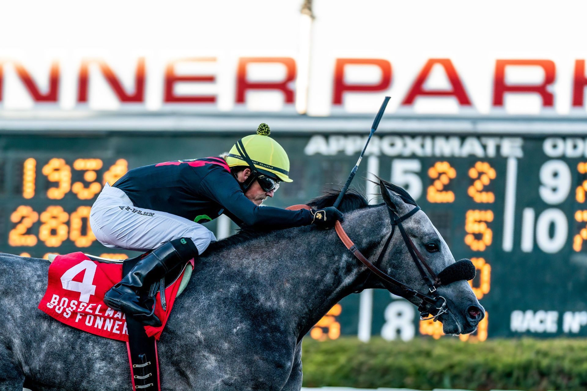 A jockey is riding a horse in front of a scoreboard.