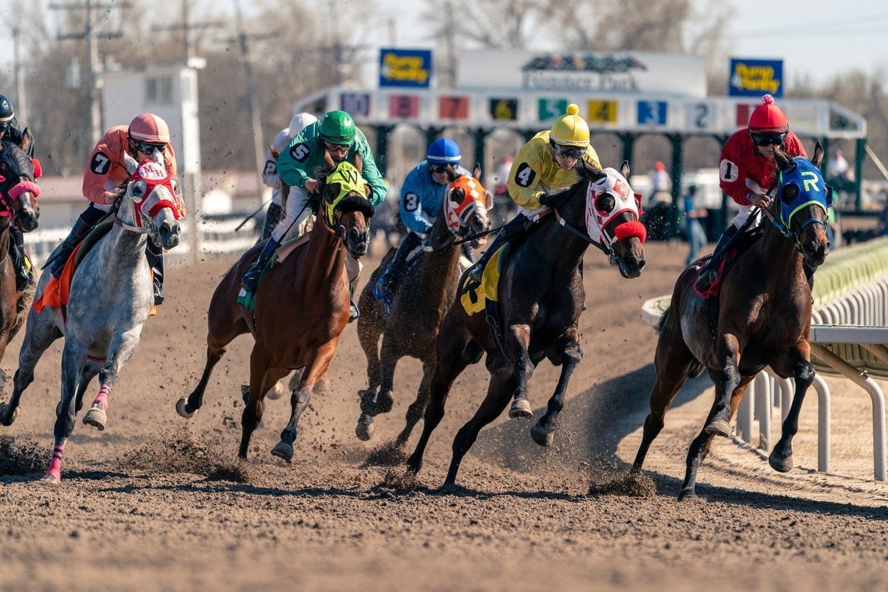 A group of jockeys are riding horses on a dirt track.
