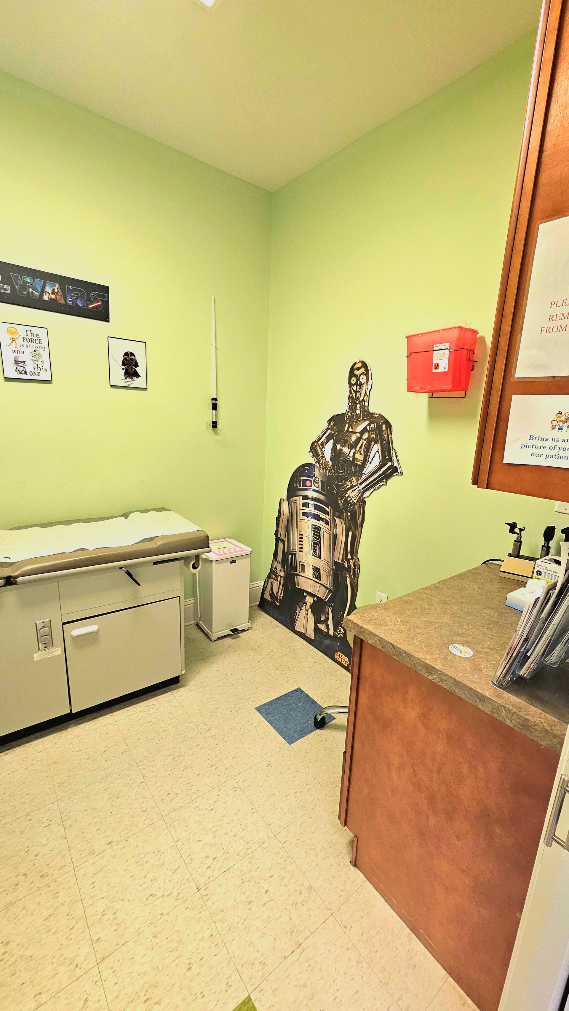 Doctor's examination room with a patient bed, cabinets, and a Star Wars character cutout. Green walls.