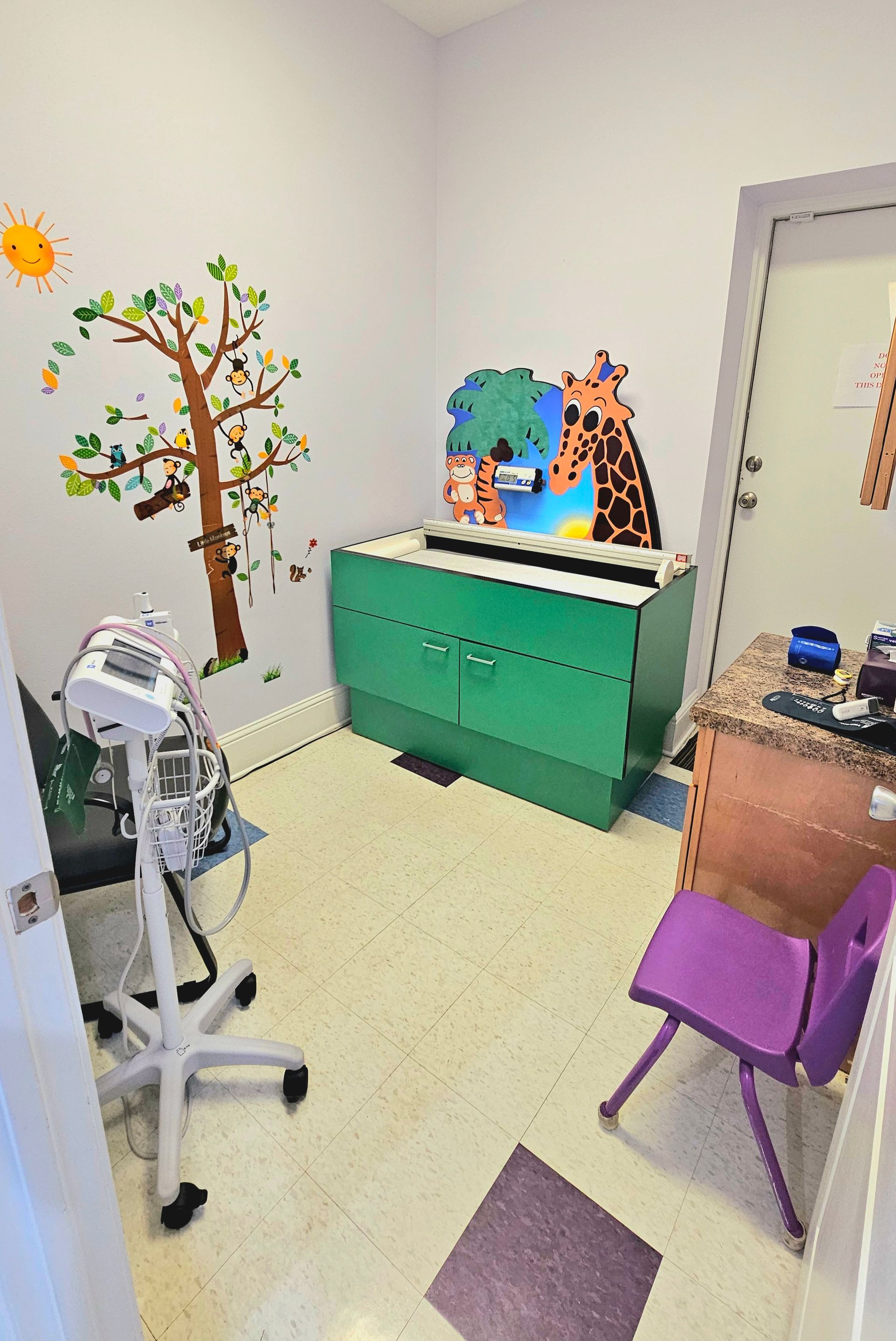 A small child's room with green cabinet, purple chair, and tree wall decals.