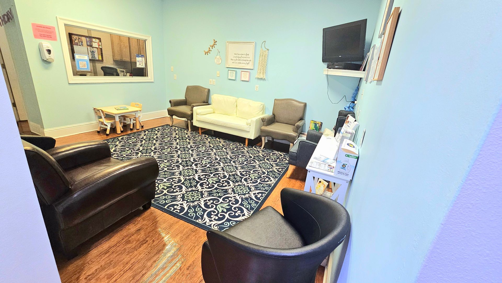 Waiting room with chairs, a couch, a rug, and a television. The walls are blue.