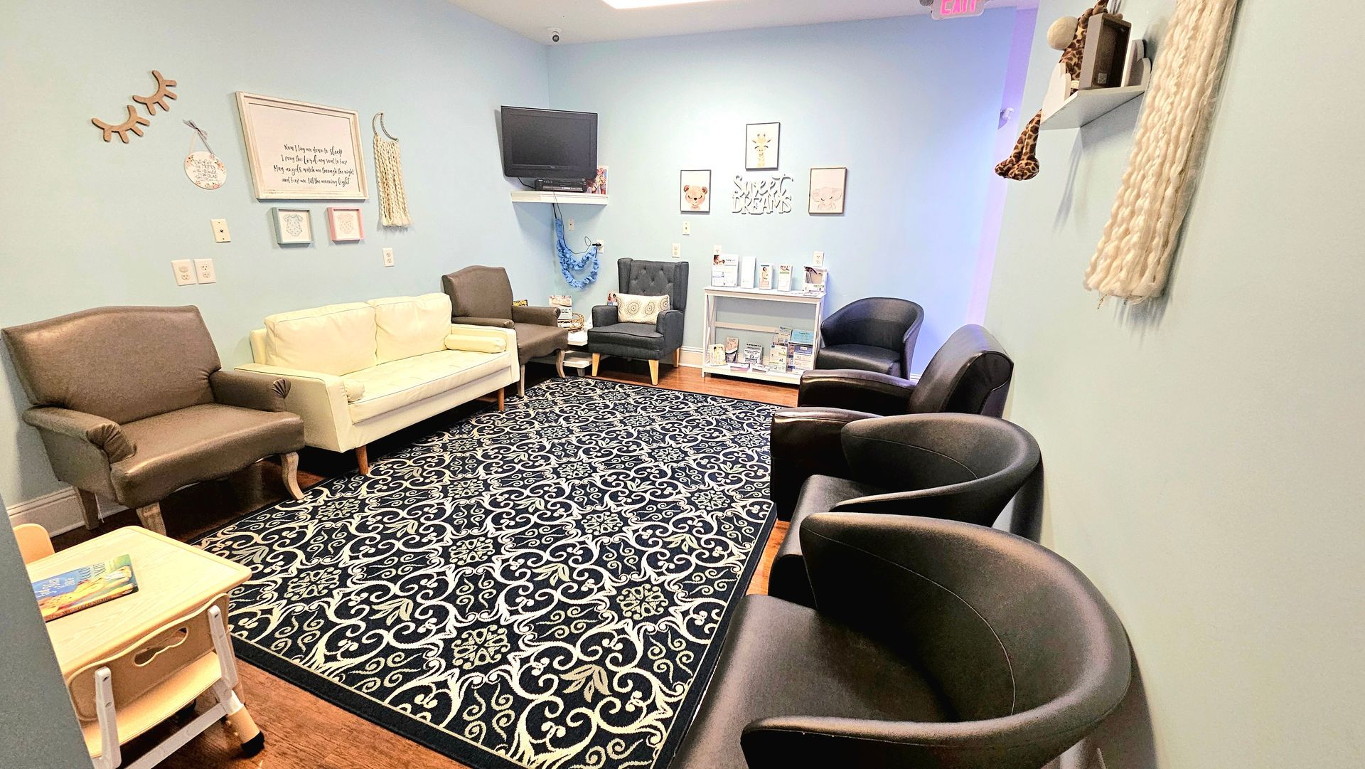 Waiting room with couches, chairs, blue walls, patterned rug, and wall decor.