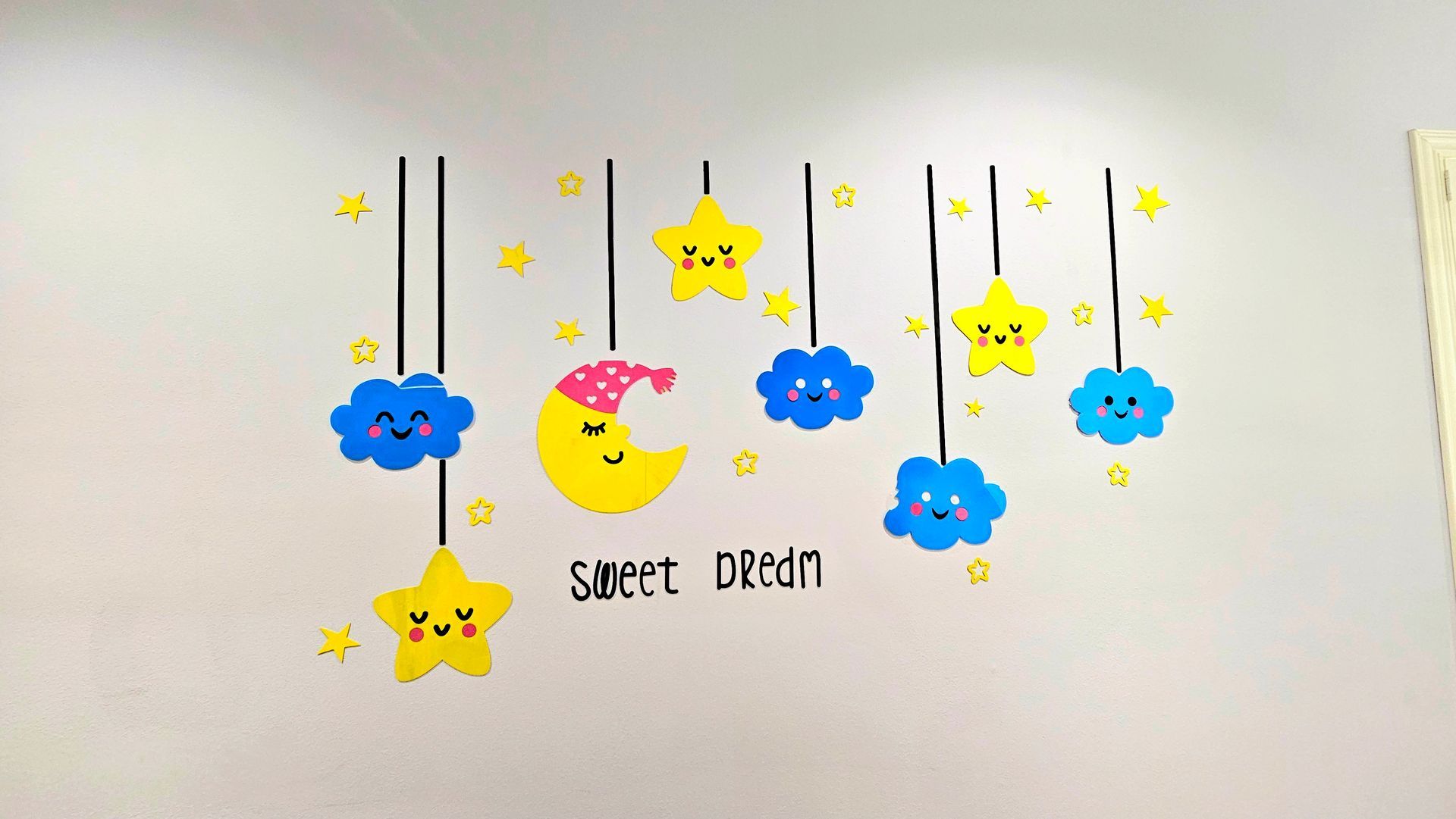 Wall art with hanging stars, clouds, and crescent moon, all with smiling faces. Text reads 