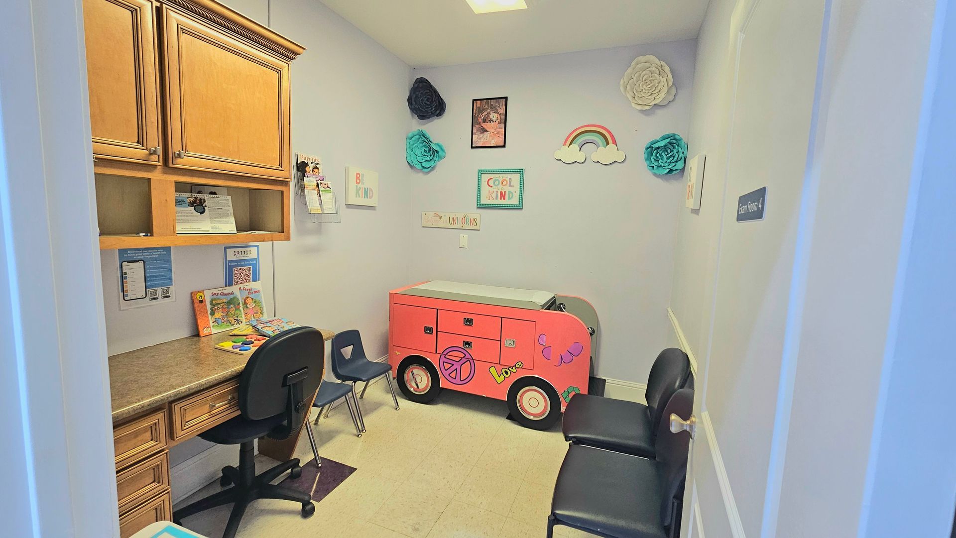 A colorful doctor's exam room with a desk, child-sized chairs, and a whimsical changing table shaped like a bus.