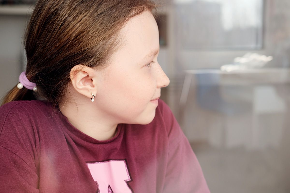 Girl with brown hair in ponytail, wearing a burgundy shirt, looking right, small earrings.