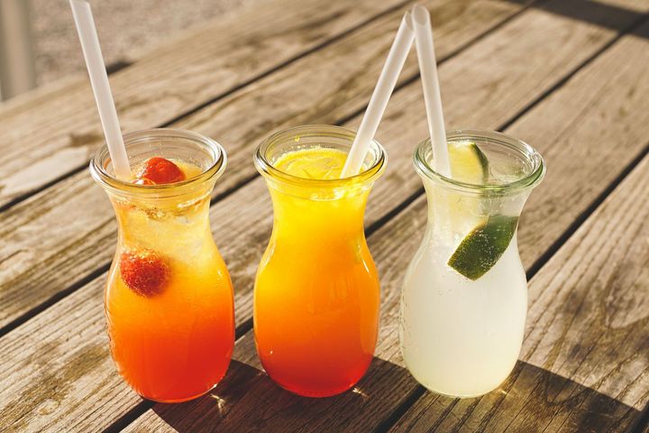 Three colorful drinks in glass jars with straws on a wooden table.