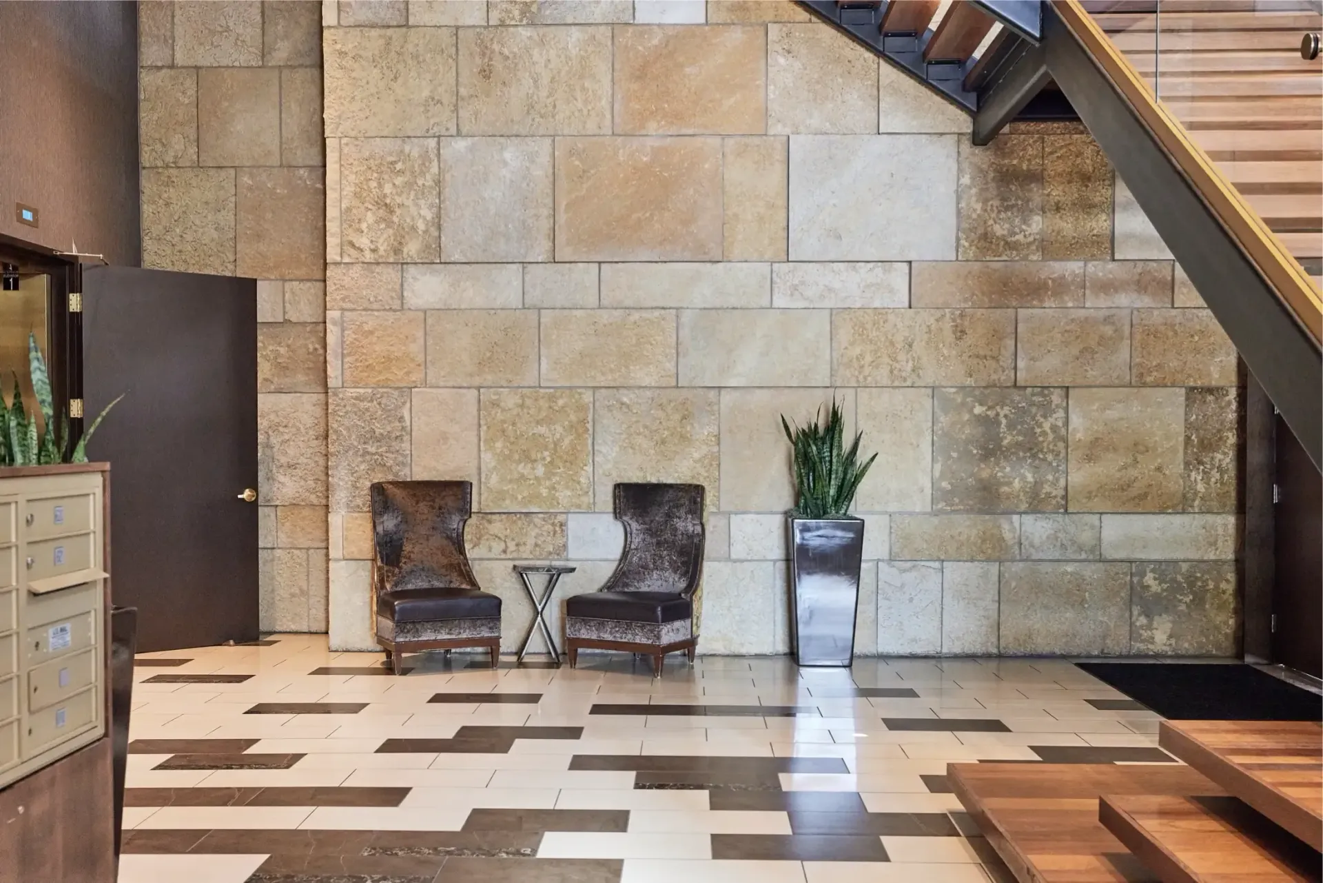 Lobby area with a stone accent wall, two chairs, small table, and plants at The Walkway, which offers Minneapolis apartments for rent.