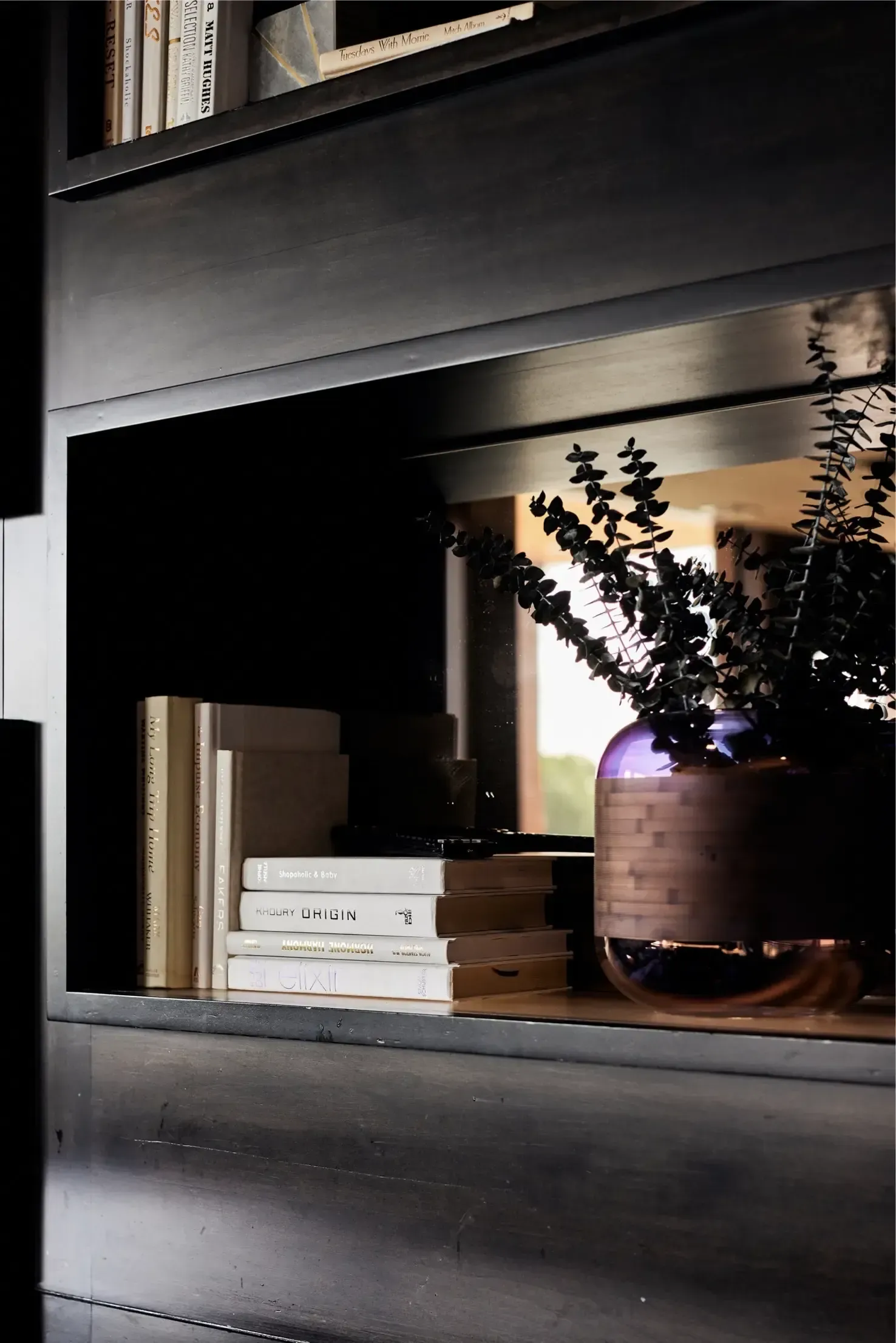 Dark built-in bookshelf with stacked books and a purple vase with greenery at The Walkway, which offers Minneapolis apartments for rent.