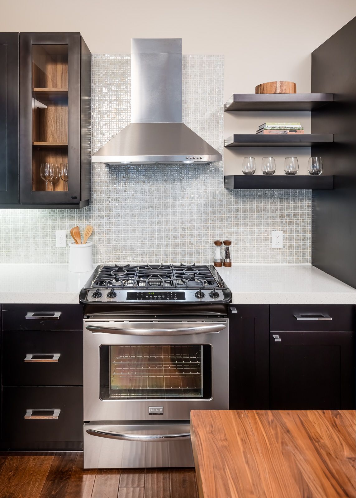 Modern kitchen with stainless steel oven and range hood, black cabinets, and mosaic tile backsplash at The Walkway, which offers apartments in Uptown Minneapolis, MN.