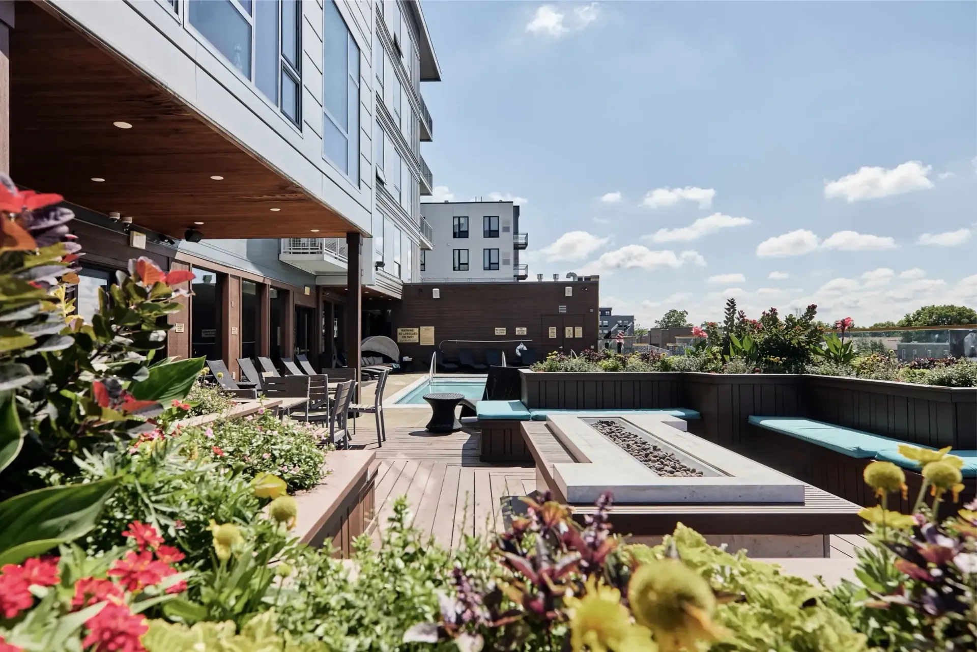 Rooftop pool area with lounge chairs and lush plants beside a modern apartment building at The Walkway, which offers apartments for rent in Minneapolis, MN.