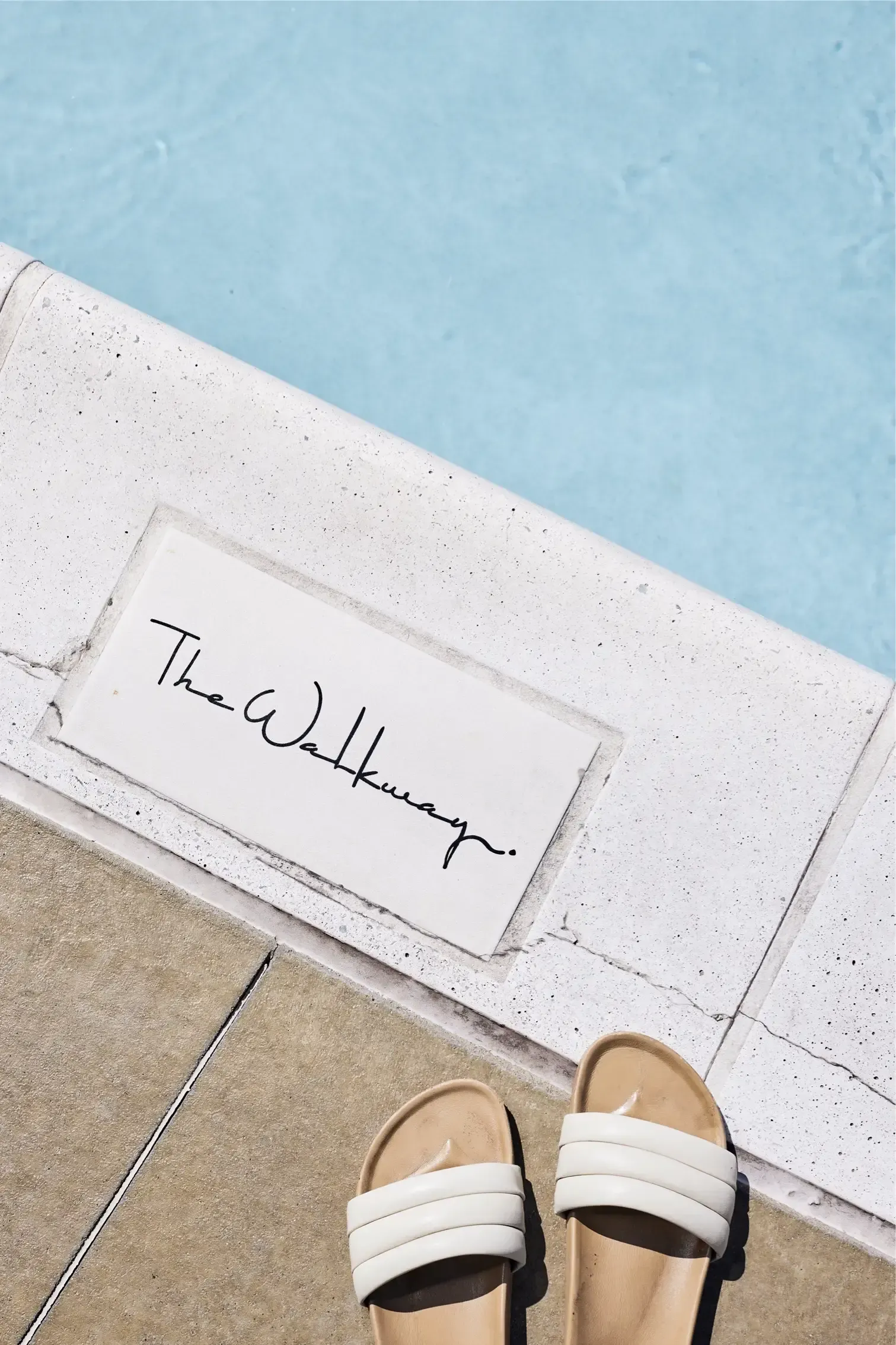 Poolside edge with blue water, white sandals, and a sign reading 'The Walkway'.