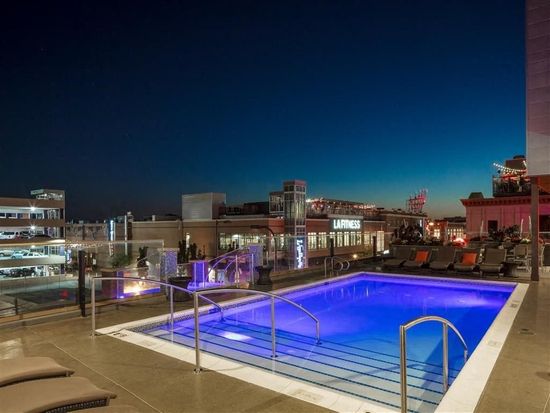 Rooftop pool at dusk, blue water, lounge chairs, city skyline in the background.