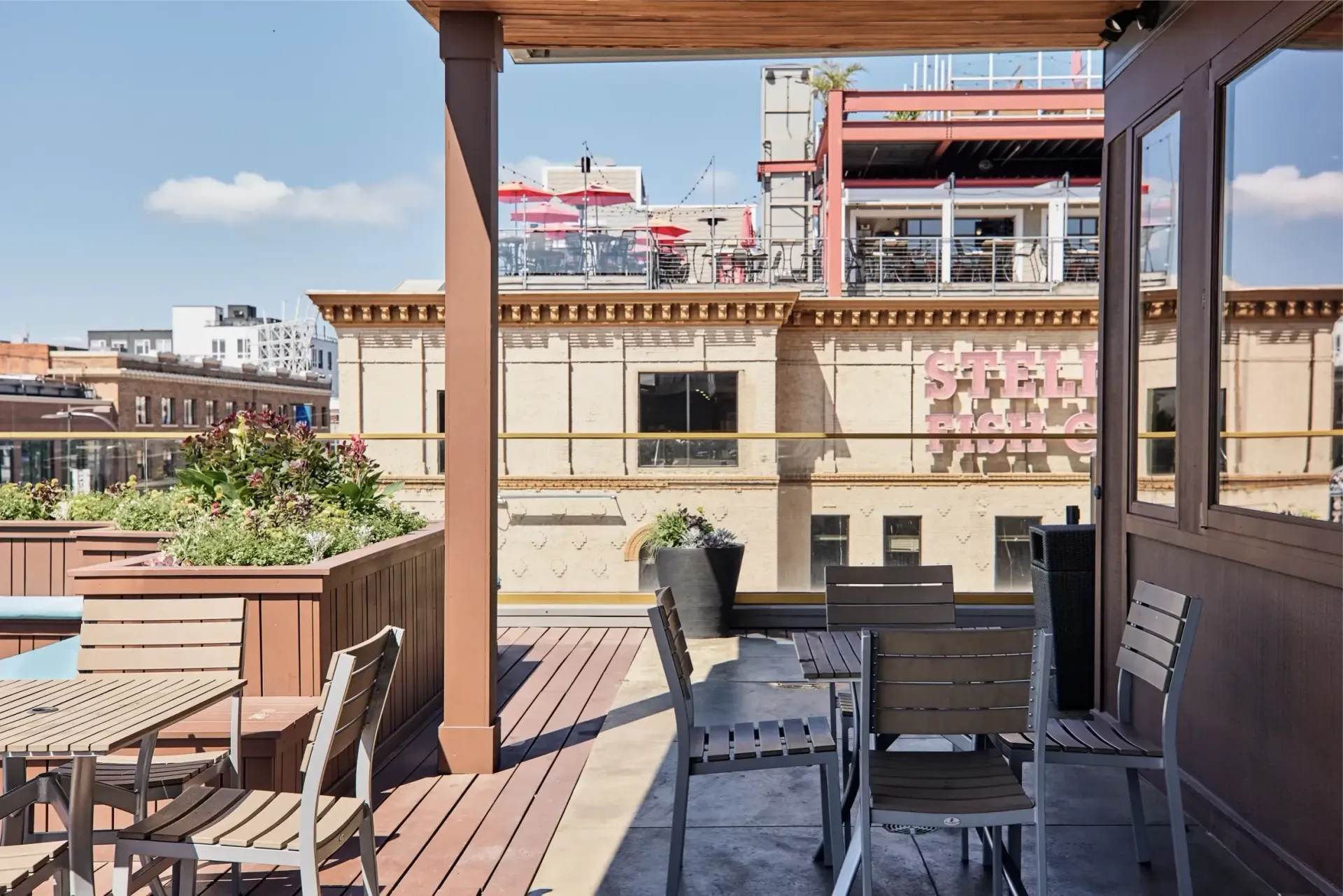 Rooftop communal terrace with tables, chairs, planters, and city buildings in the background at The Walkway, which offers apartments in Minneapolis, MN.