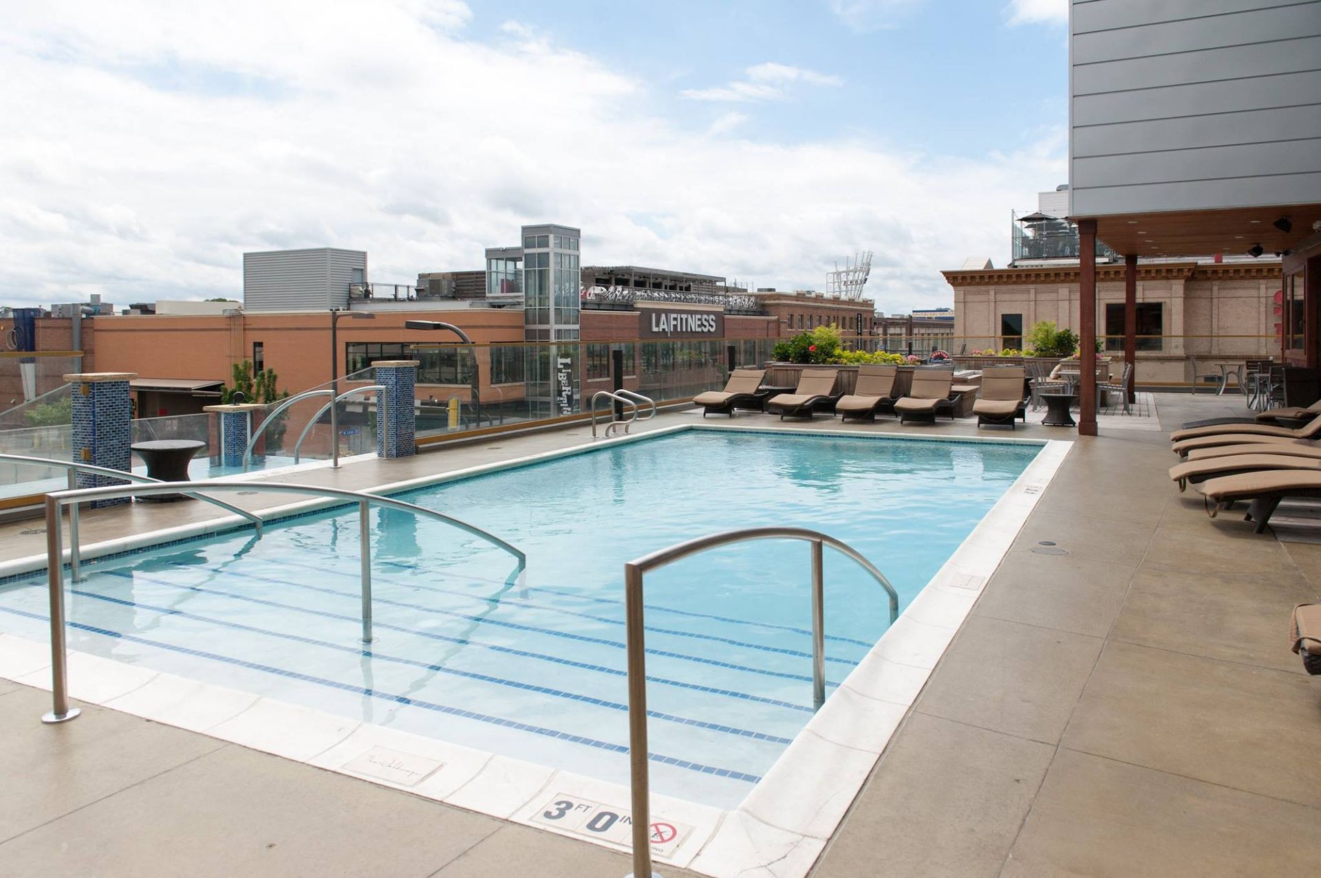 Rooftop pool with chaise lounges. City buildings in the background under a cloudy sky The Walkway Apartments.