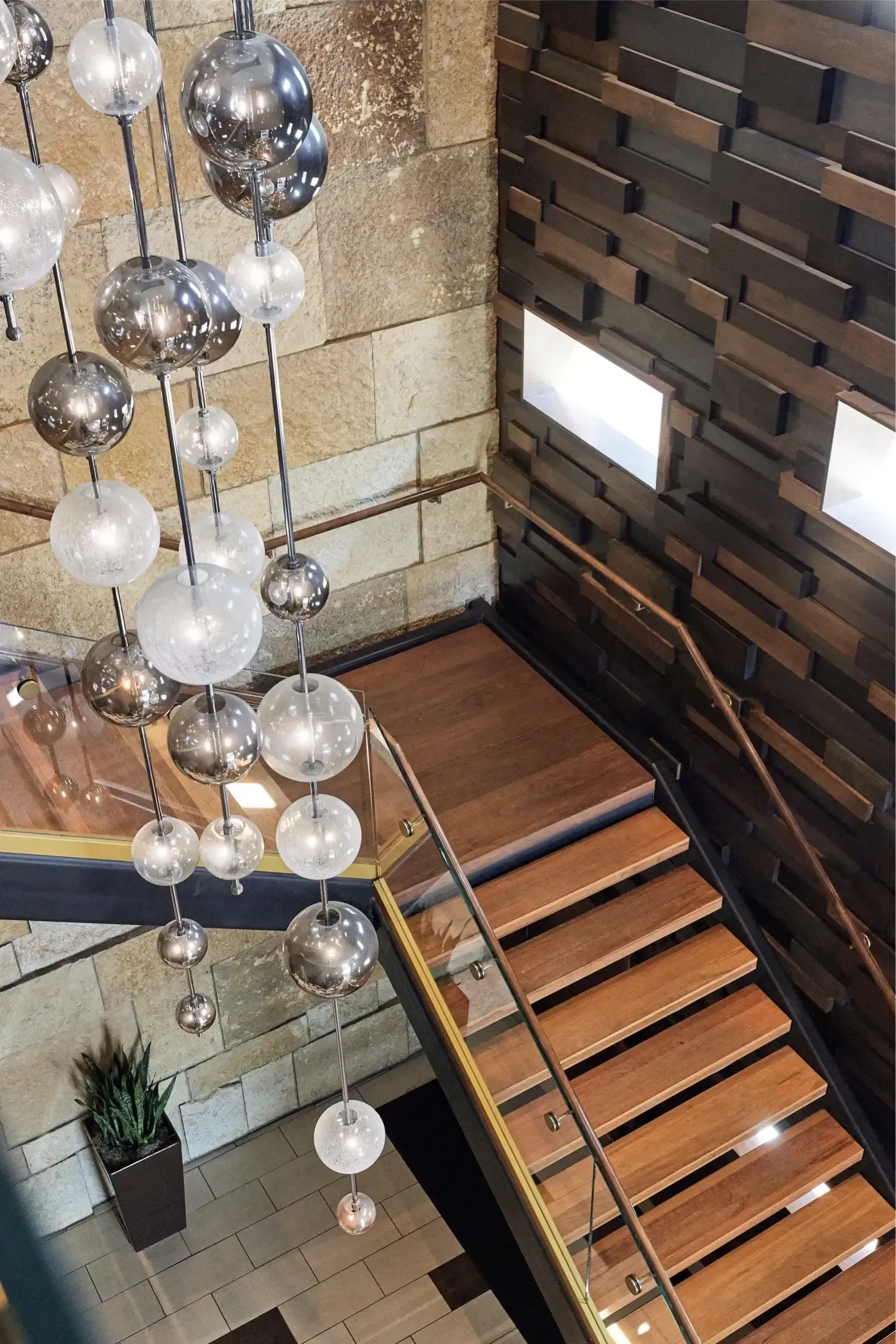 Interior staircase in a modern building lobby with glass railing and hanging spherical chandelier at The Walkway, which offers Minneapolis apartments for rent.