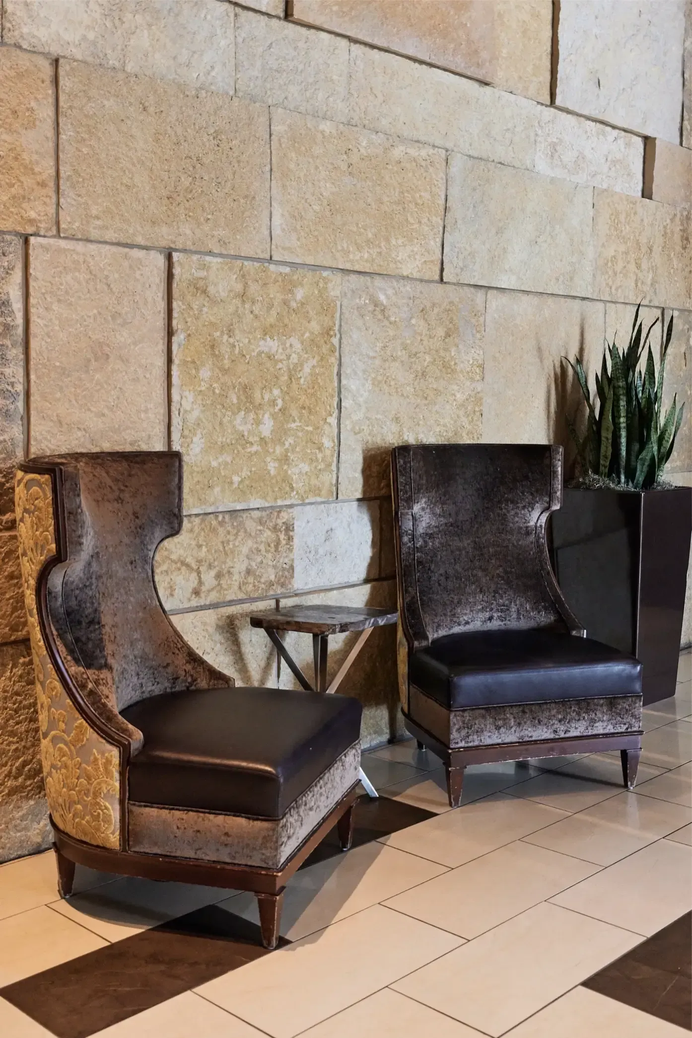 Two dark upholstered lounge chairs with a small side table in a stone-walled lobby at The Walkway, which offers pet-friendly apartments in Minneapolis, MN.