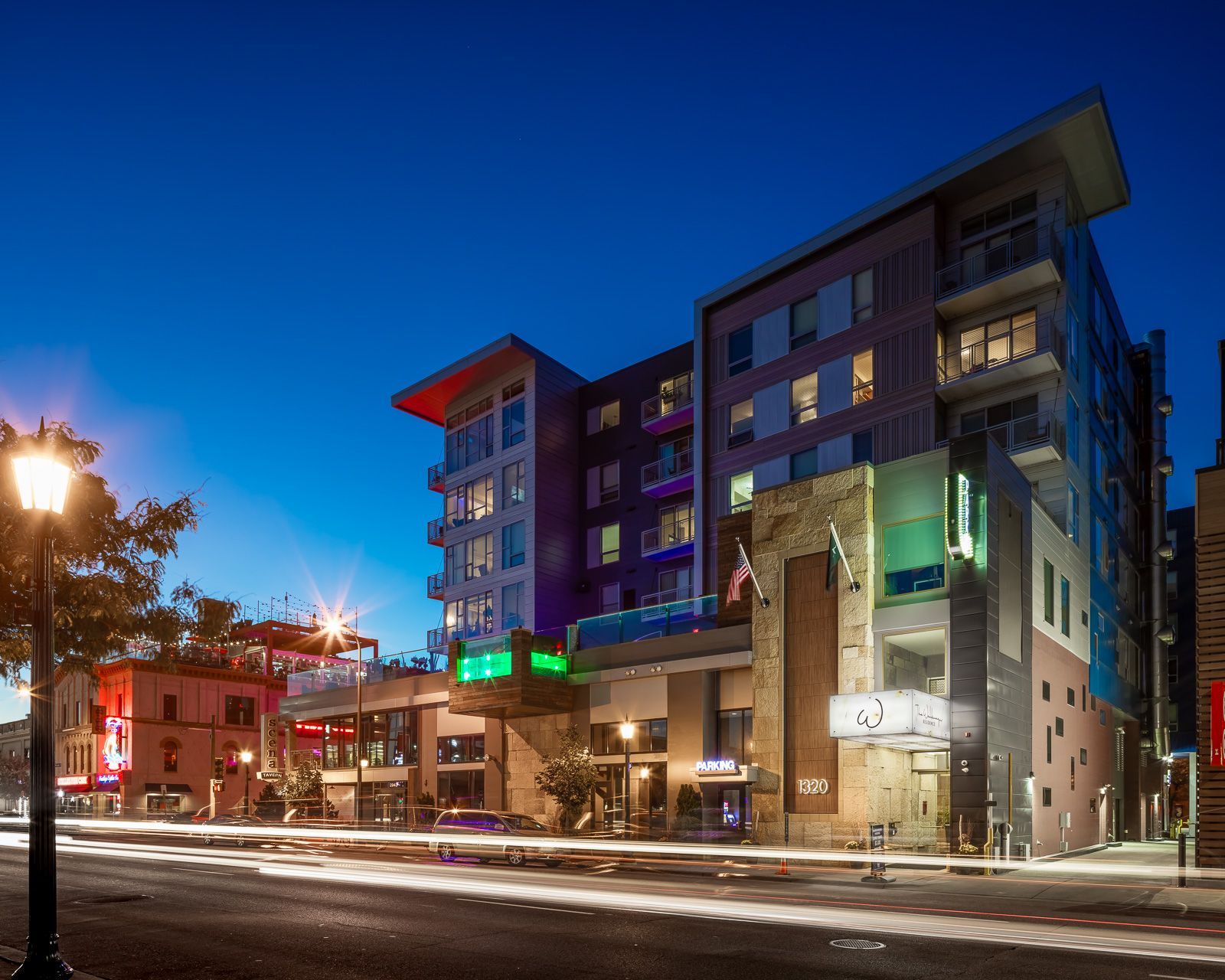 Nighttime exterior view of a modern apartment building with lit storefronts and street at The Walkway, which offers apartments in Minneapolis, MN.