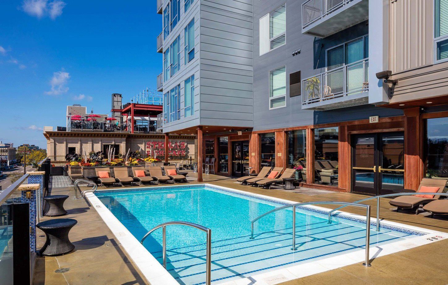 Rooftop pool with lounge chairs at apartment building under blue sky The Walkway Apartments.