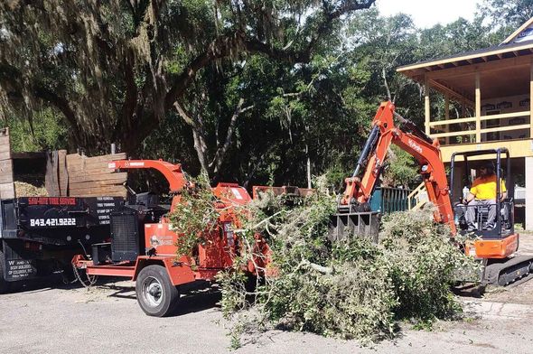 A tree chipper and an excavator are parked in front of a house.