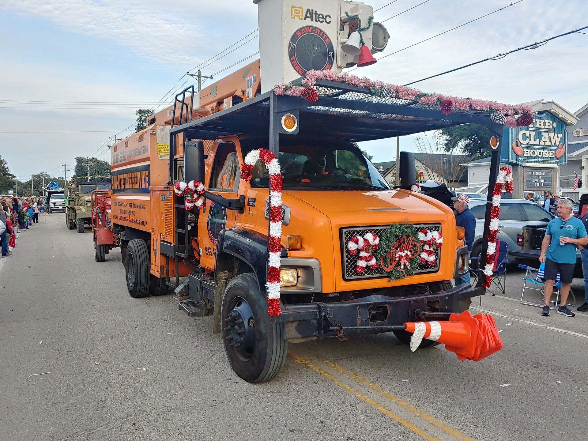 A large orange truck is decorated for christmas in a parade.