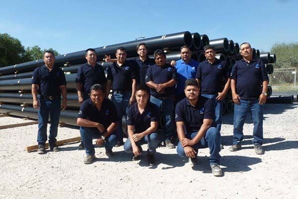 Un grupo de hombres posando para una foto frente a una pila de tuberías.