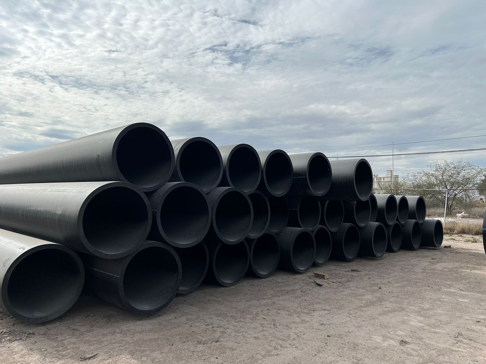 Una pila de tubos negros apilados uno encima del otro en un campo de tierra.