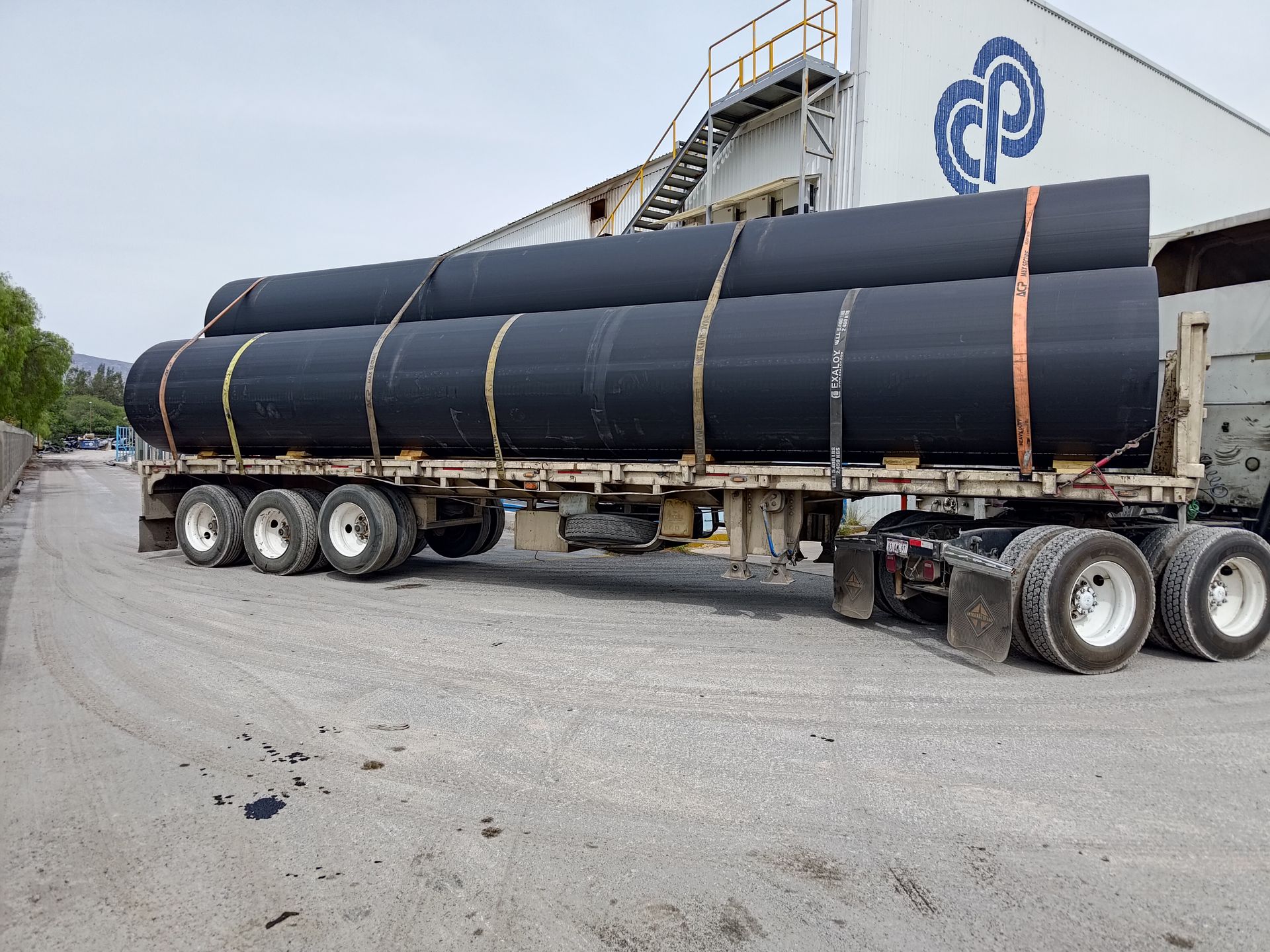 Un camión transporta una pila de tubos negros en un remolque.