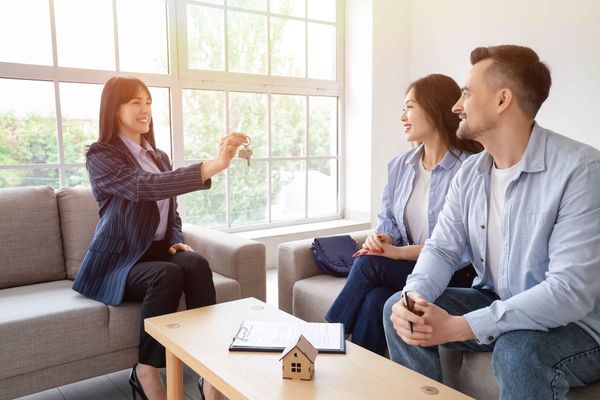Un agent immobilier remet les clés à un couple dans un salon lumineux.